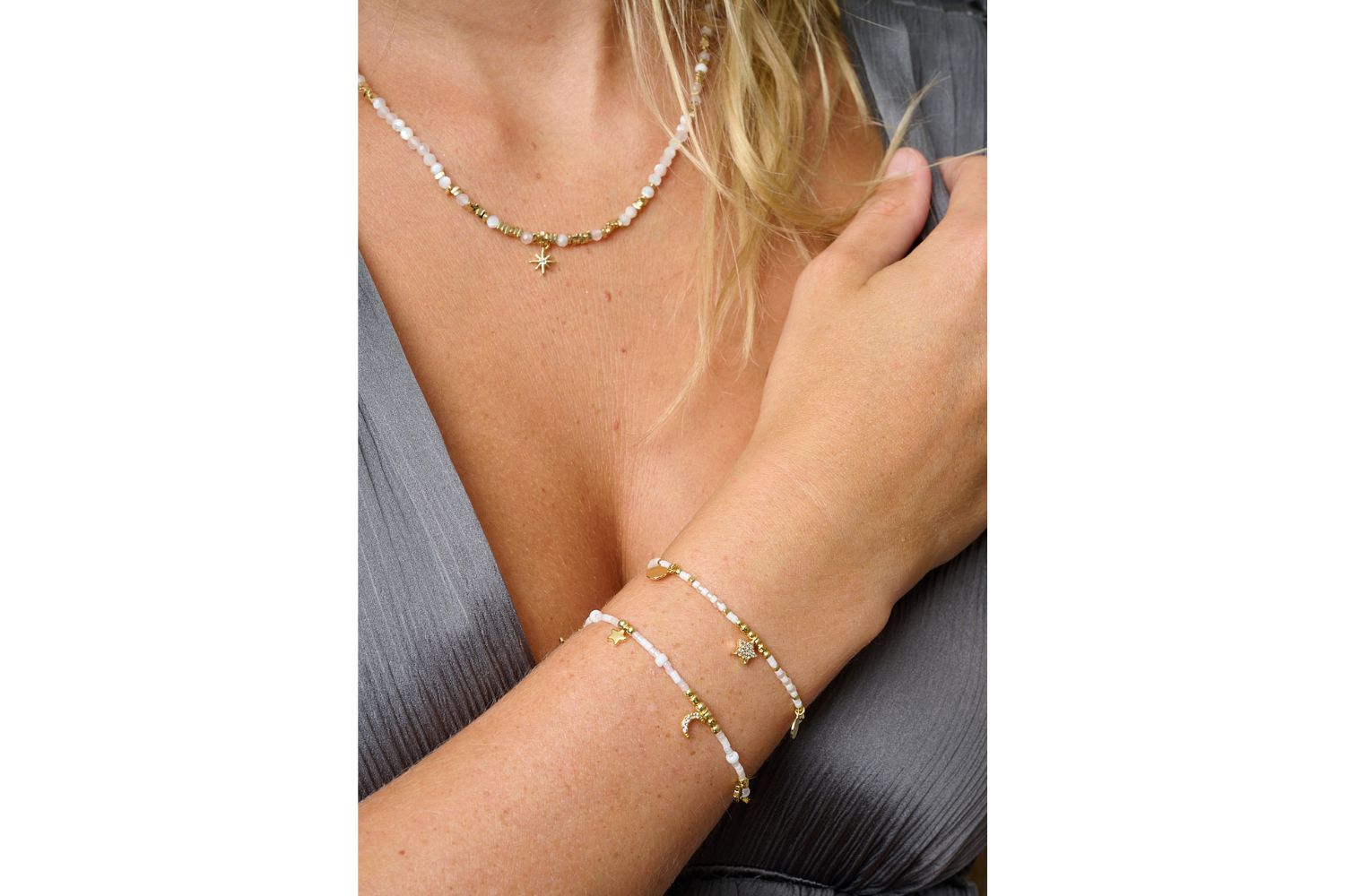 Mondesi white and gold stacking bracelets styled on wrist, soft ivory beads, crescent moon and star charms catching golden light.