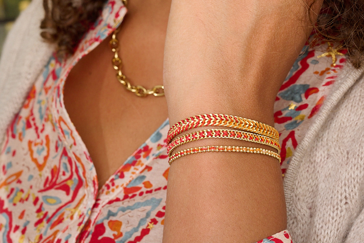 Banda Sunset Gold Stacking Bracelets, fiery red-to-orange ombré woven designs with radiant gold chains in a three-bracelet stack.