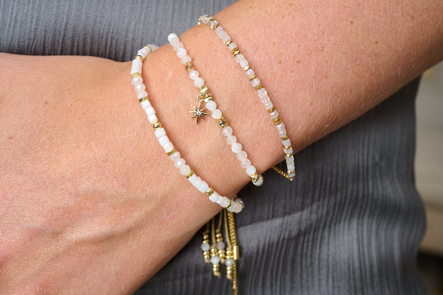 Casaya rainbow moonstone and gold stacking bracelets styled on wrist, luminous moonlight tones with golden glow.