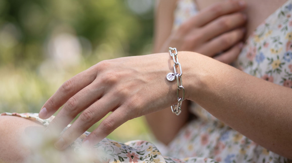 Close-up of a female model wearing a luminous silver chain bracelet on her wrist outdoors, highlighting craftsmanship and shimmer in natural daylight.