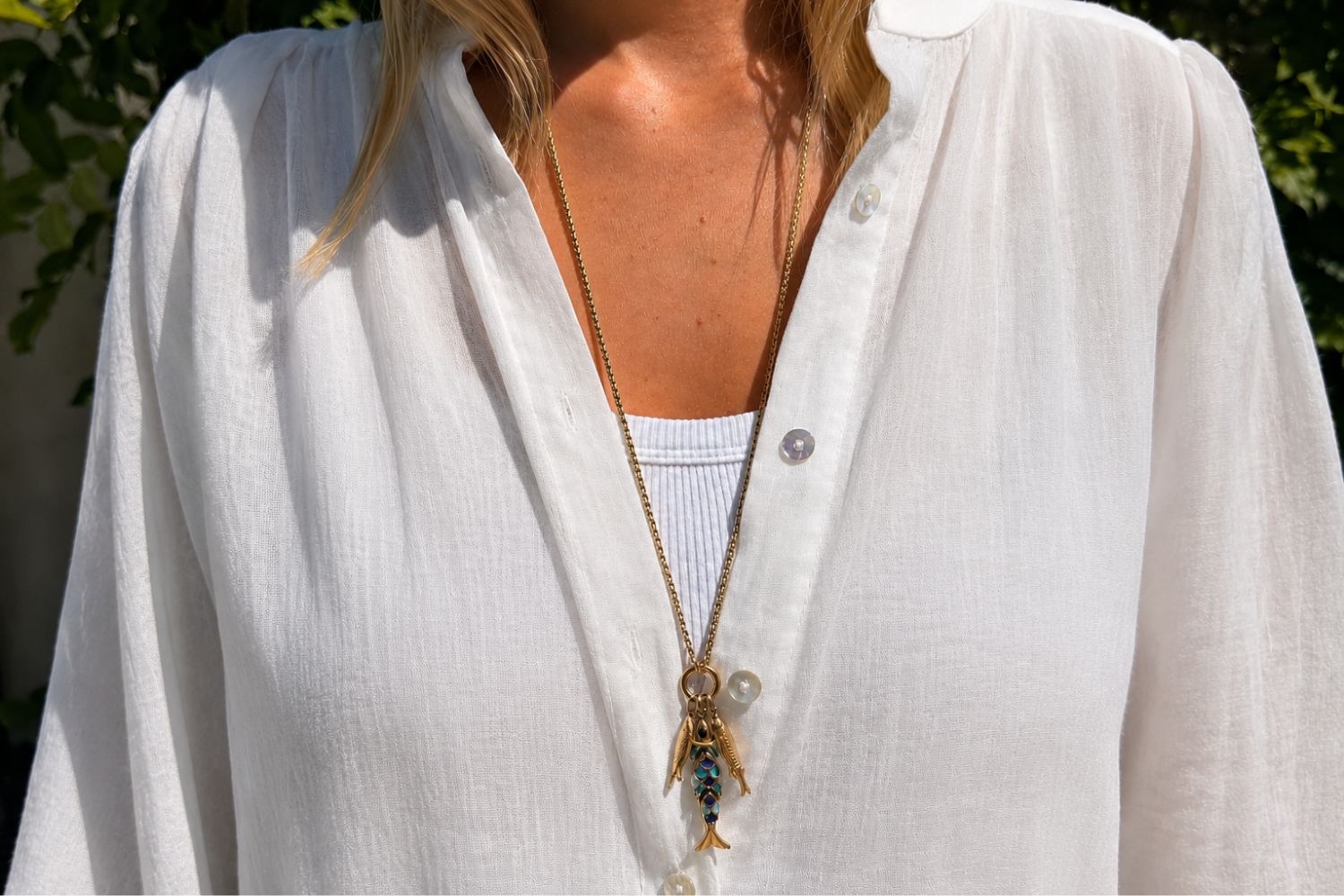 Minami Blue Ombre Waterproof Long Gold Fish Cluster Necklace worn layered over clothing, showcasing a trio of fish charms including a blue ombré enamel fish on a long waterproof 14k gold PVD charm carrier chain inspired by the ocean.