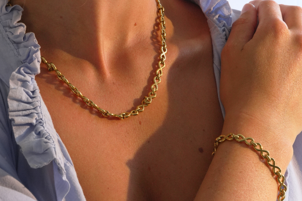 Octavia Gold Infinity Link Bracelet worn layered with polished gold infinity chain links, a waterproof 14k Gold PVD stainless steel finish and an adjustable lobster clasp.