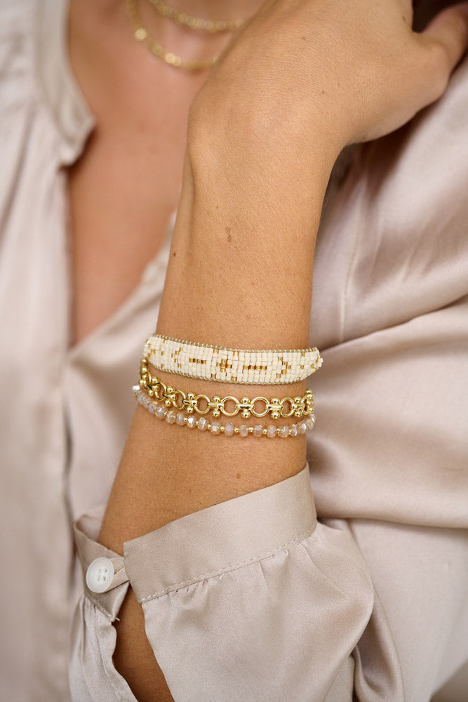 The Palawan Champagne Gold Bracelet Stack styled on the wrist, showcasing the cream Miyuki beads, gold infinity chain links, and smoky crystals for a touch of luxury.